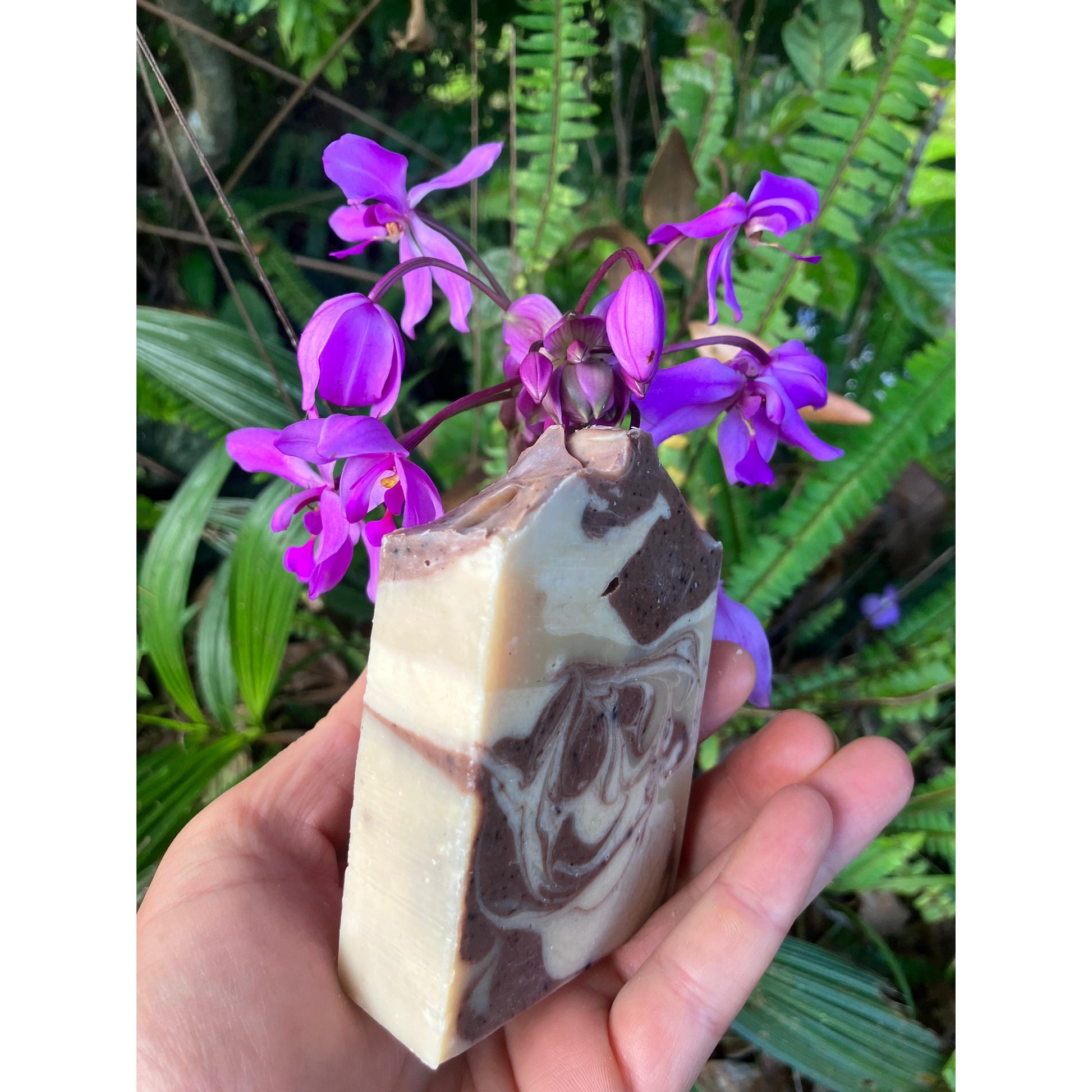 Hand holding a marbled soap bar with purple flowers in the background