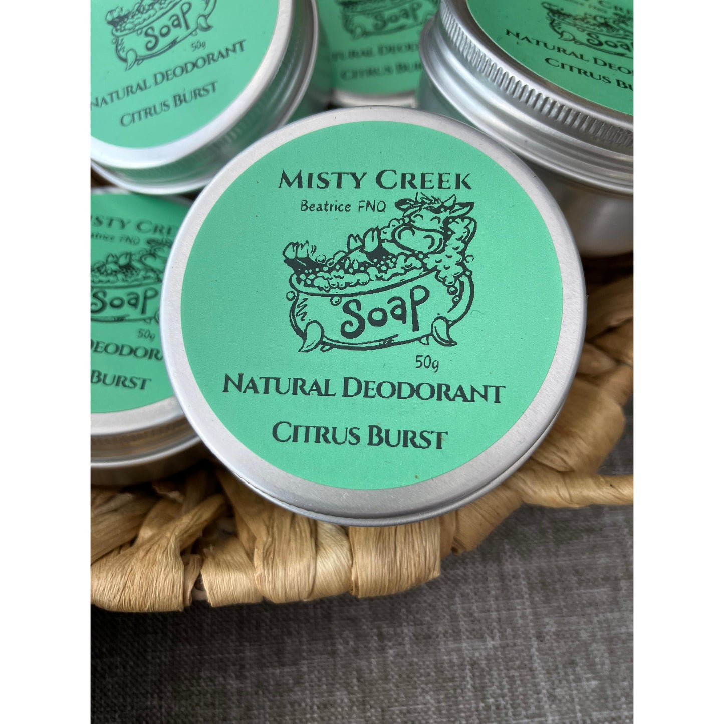 Misty Creek Soap natural deodorant tins with green labels on a woven mat.