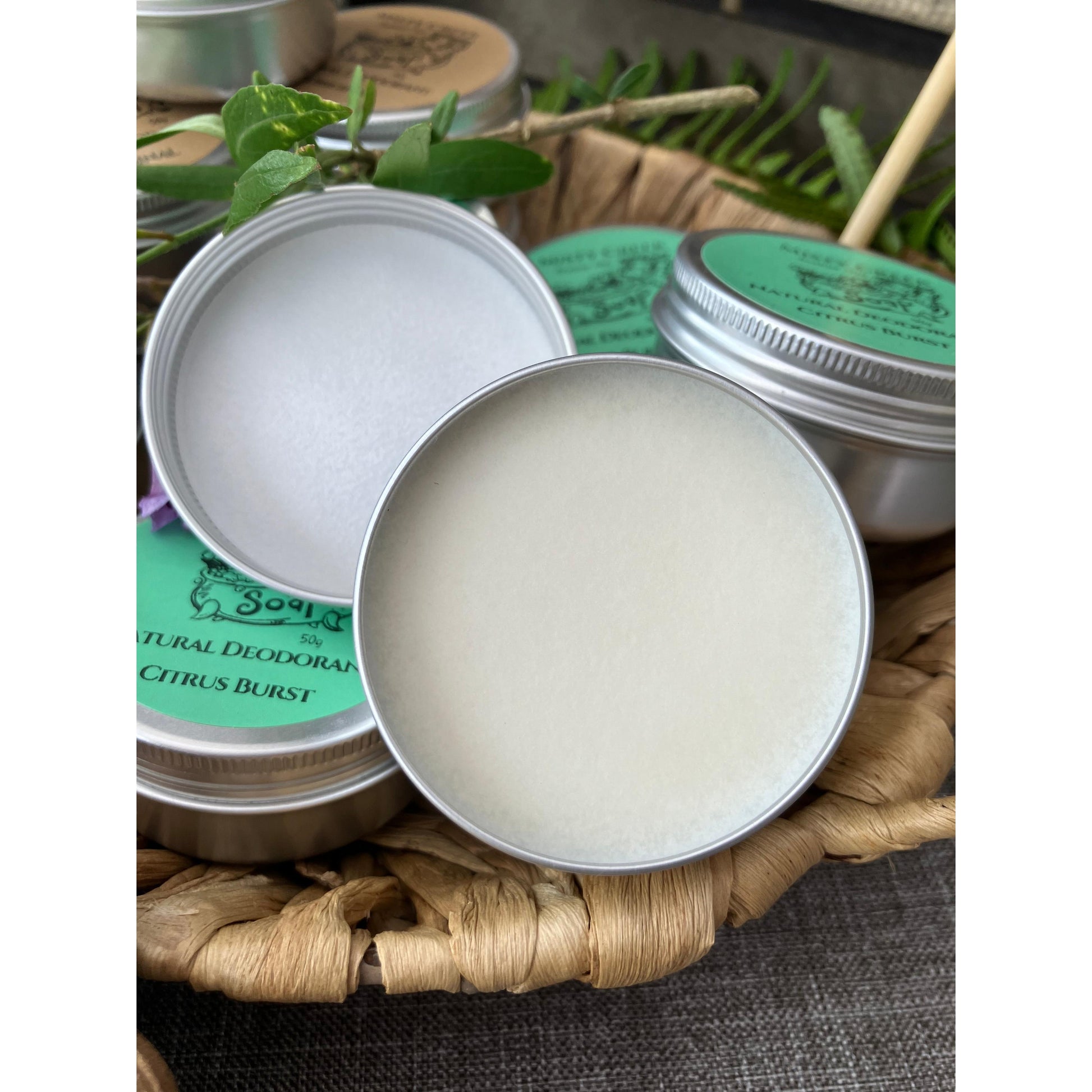 Multiple tins of natural deodorant with green labels on a woven mat.