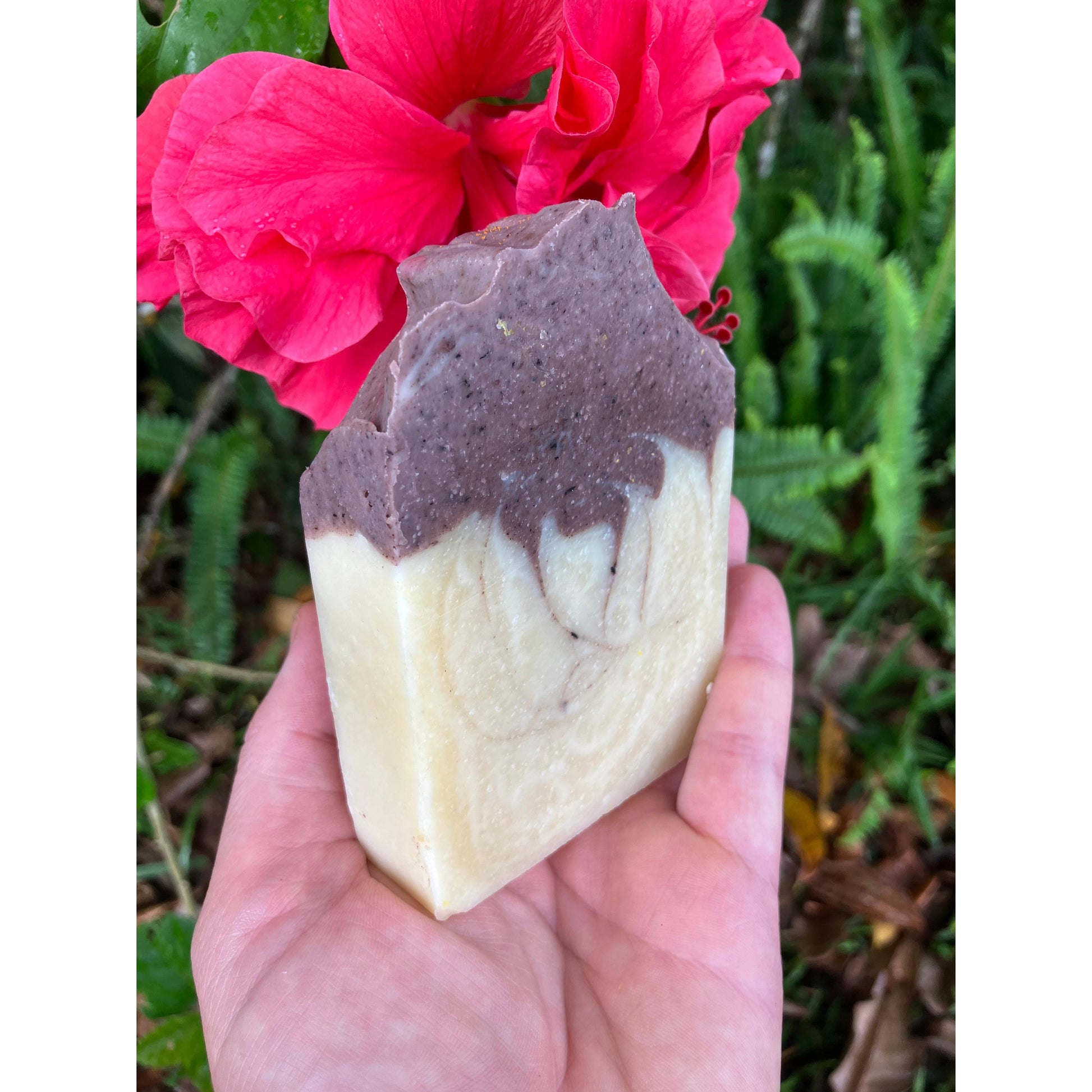 Hand holding a marbled deep purple organic lavender soap bar with a pink flower in the background